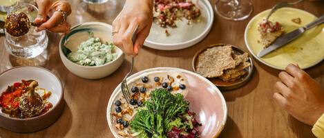 Una mesa de comedor con diversos platos, incluyendo un plato de brócoli y nueces, y varias copas de vino.