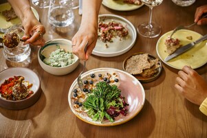 Una mesa de comedor con diversos platos, incluyendo un plato de brócoli y nueces, y varias copas de vino.