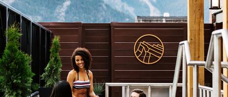 Una piscina en la azotea con vista a la montaña, terraza de madera y un logotipo en la pared.