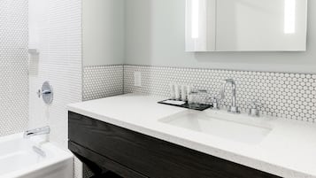 A modern bathroom with a large mirror, white sink, and shower.