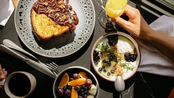 Una mesa con tostadas, fruta, yogur y un vaso de zumo de naranja para el desayuno.