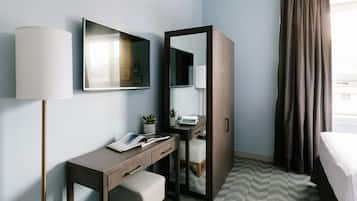 Habitación de hotel con escritorio, silla, espejo, armario y cama.