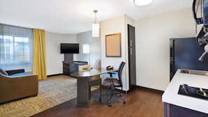 Habitación de hotel con una mesa de comedor, sofá, televisor, escritorio y refrigerador.