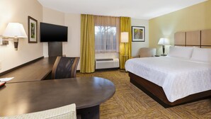 Habitación de hotel con cama, escritorio, silla, televisor y ventana con cortinas.