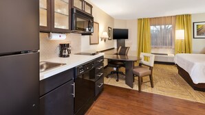 Una habitación de hotel compacta con kitchenette, una cama, un escritorio y un televisor.