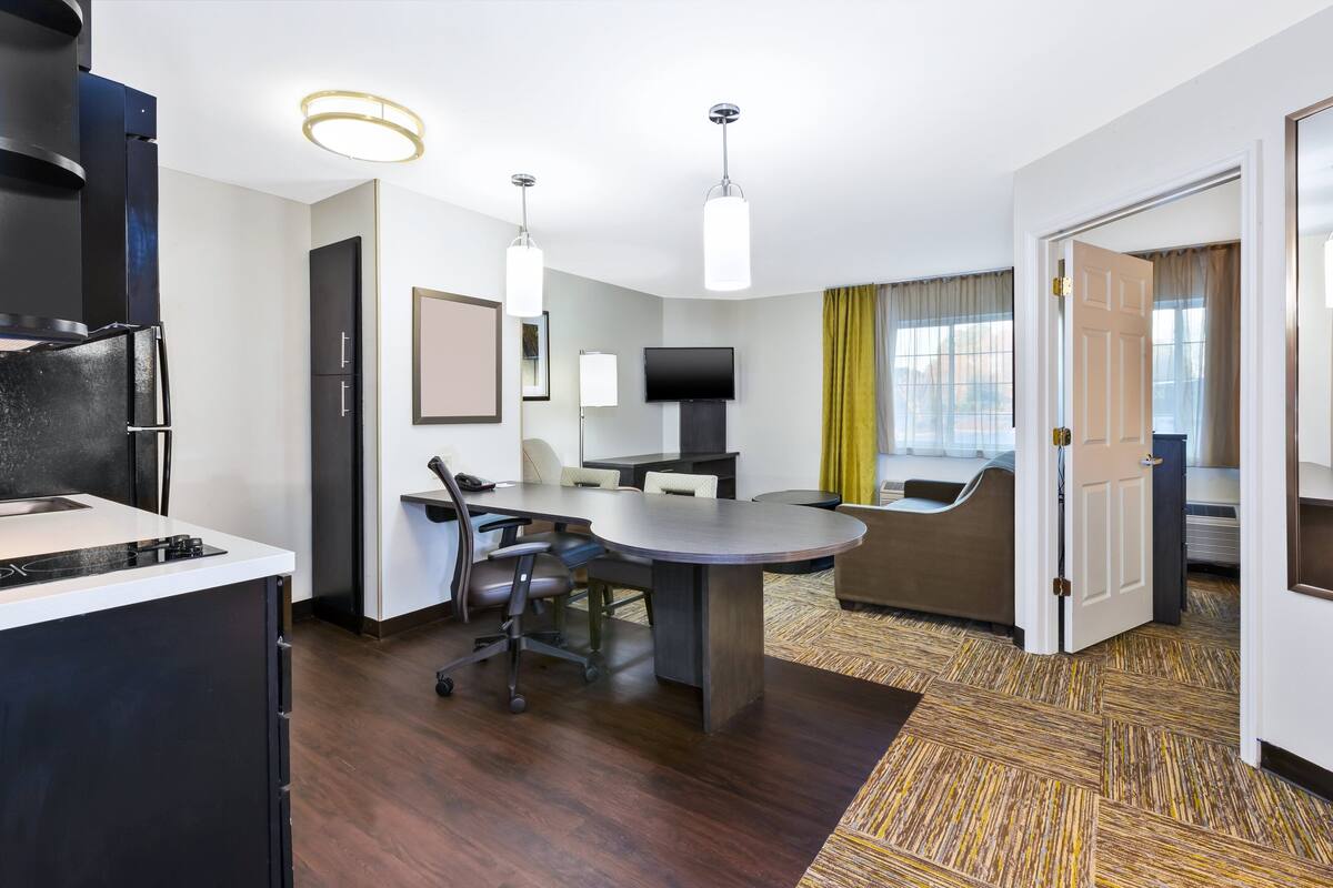 A modern hotel room with a kitchen area, a dining table, and a sofa.