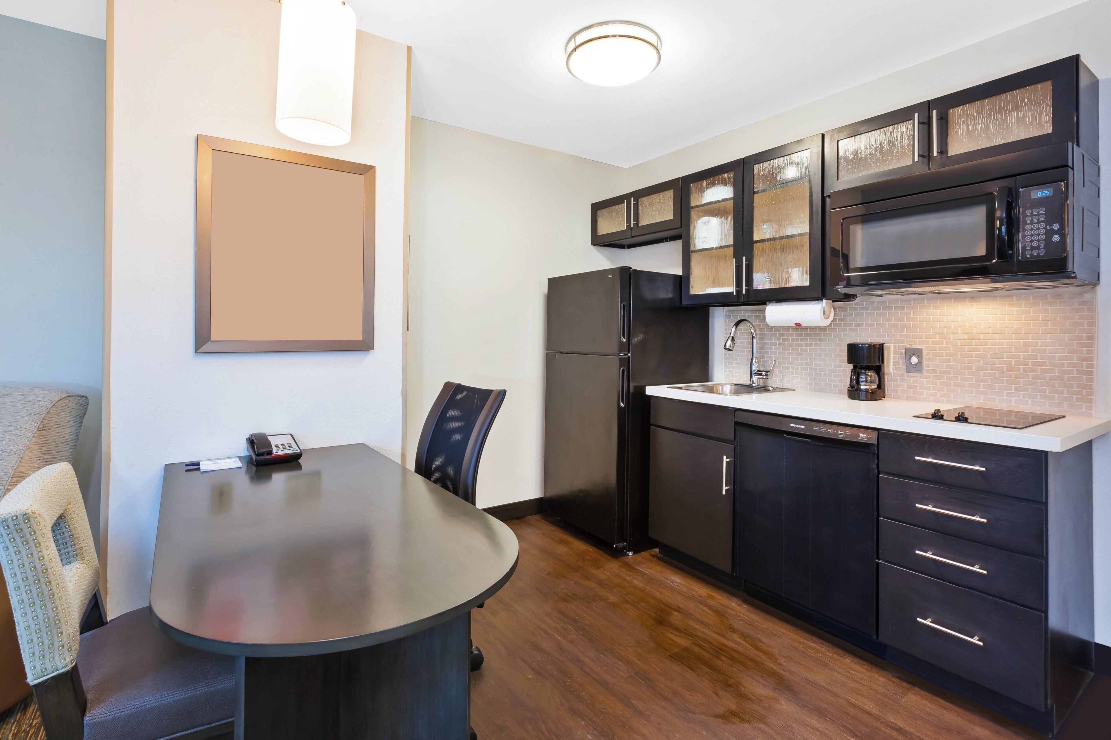 A modern kitchen with a black refrigerator, a microwave, and a dishwasher. There is a dining table with chairs and a light fixture above it.
