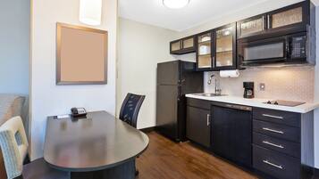 A modern kitchen with a black refrigerator, a microwave, and a dishwasher. There is a dining table with chairs and a light fixture above it.
