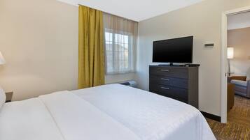 A hotel room with a bed, a flat-screen TV, a dresser, and a window with curtains.