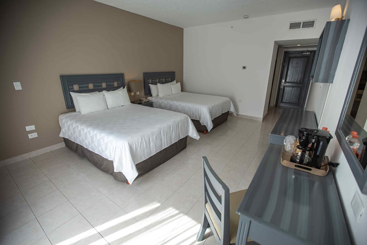 Una habitación de hotel con dos camas, un escritorio con cafetera y un espejo.