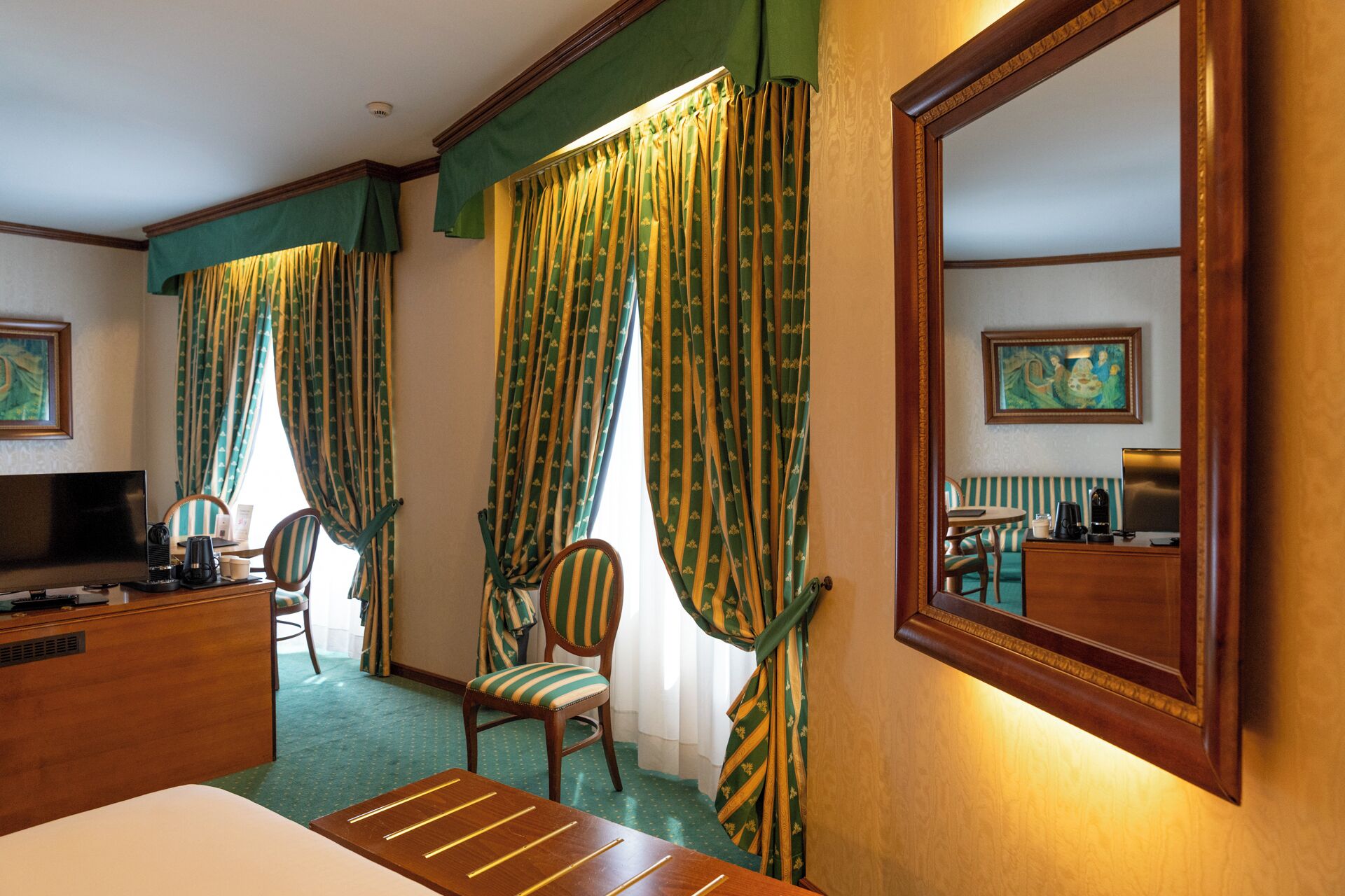 A hotel room with a bed, a desk with a computer, a chair, a sofa, and curtains.