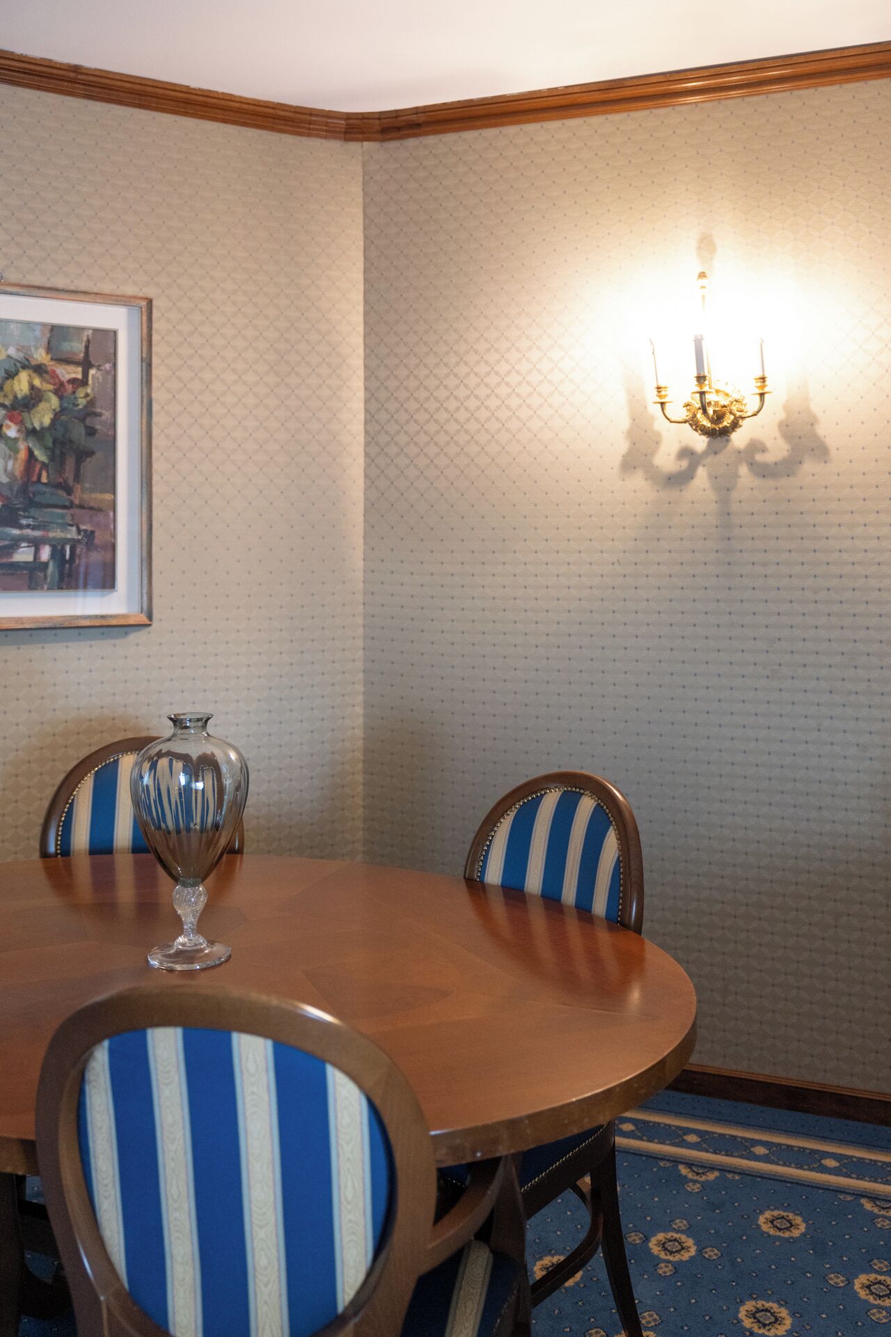 Ein Essbereich mit einem runden Tisch, Stühlen, einer Vase, einem gerahmten Bild und einer Wandleuchte.