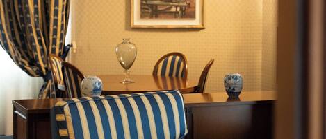 Una habitación con un sofá a rayas, una mesa de comedor con sillas, un florero y un cuadro enmarcado en la pared.