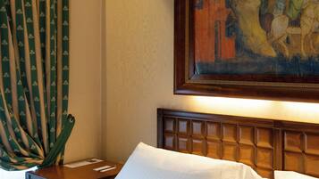 A hotel room with a large bed, a nightstand, a painting above the bed, and curtains on the window.