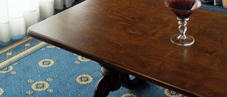 A room with a wooden table, a blue patterned carpet, a striped sofa, and a glass of red wine.