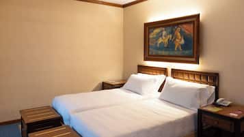 Een hotelkamer met een tweepersoonsbed, twee nachtkastjes, een bijzettafeltje met een telefoon, en een schilderij aan de muur.