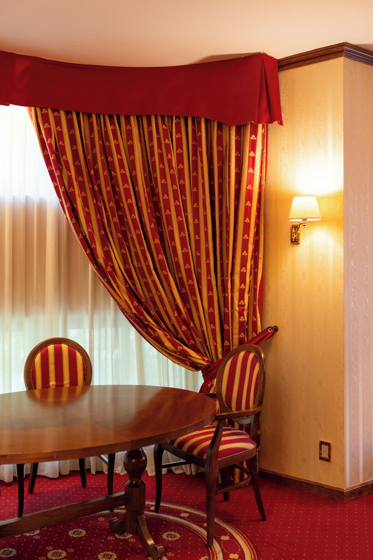 Une chambre d’hôtel avec une table à manger, des rideaux à rayures, une lampe fixée au mur et une moquette à motifs.