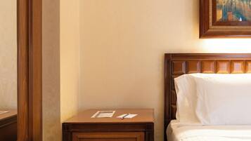 Une chambre d’hôtel avec une table de chevet en bois, un lit recouvert de draps blancs et un tableau encadré accroché au mur.