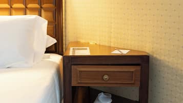 Una habitación de hotel con una cama bien hecha, una mesita de noche de madera con cajón y un papel tapiz estampado.