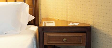 Una camera d'albergo con un letto rifatto, un comodino in legno con un cassetto e una carta da parati decorata.
