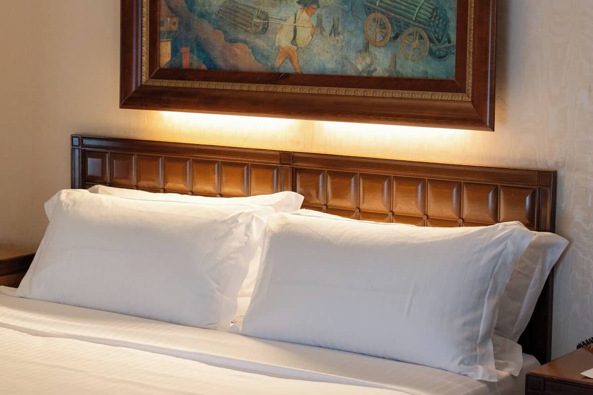 Una cama con sábanas blancas, cabecera de madera y un cuadro enmarcado encima.