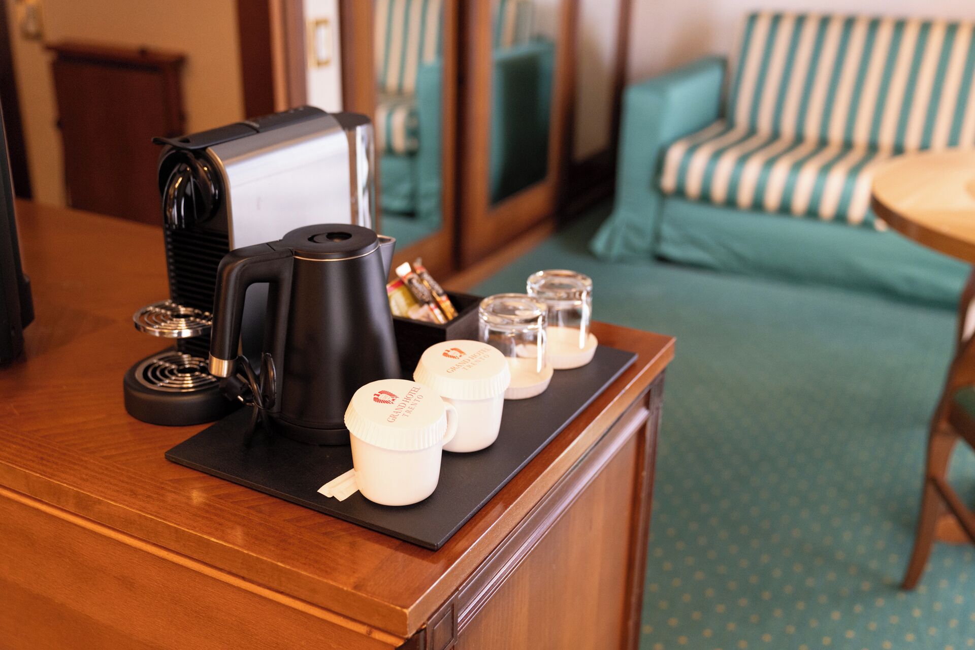A hotel reception desk with a coffee maker, a tray with three cups, and a small figurine.