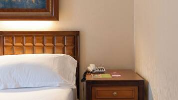 Une chambre d’hôtel avec un lit, une table de chevet en bois avec un téléphone et un tableau au-dessus du lit.