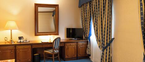 A hotel room with a bed, a desk with a lamp, a chair, a television, and curtains.