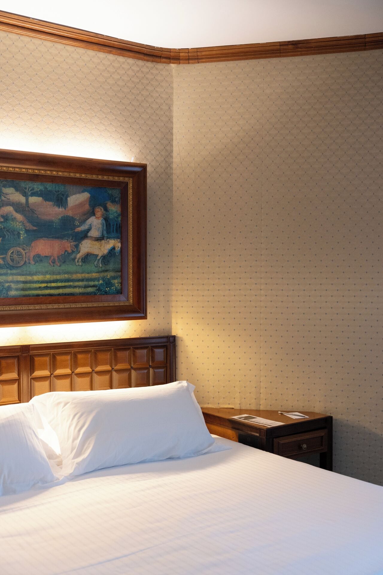 A hotel room with a bed, a nightstand, and a painting on the wall.