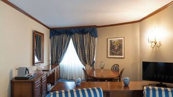Une chambre d’hôtel comprenant un coin repas, une télévision, un tableau et un lustre.
