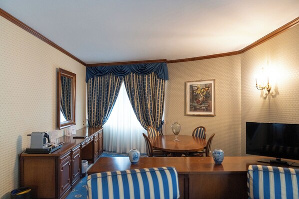 A hotel room with a dining area, a TV, a painting, and a chandelier.