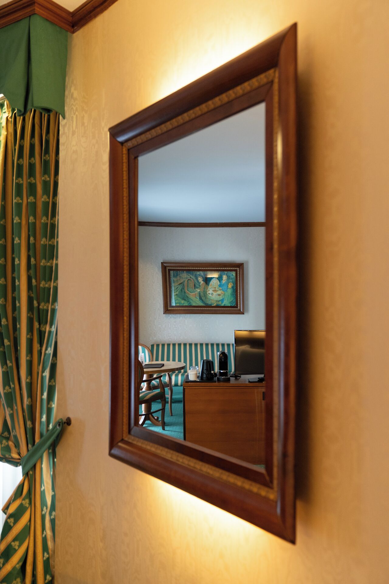 A mirror with a wooden frame, a painting on the wall, a sofa, a table, and a chair.