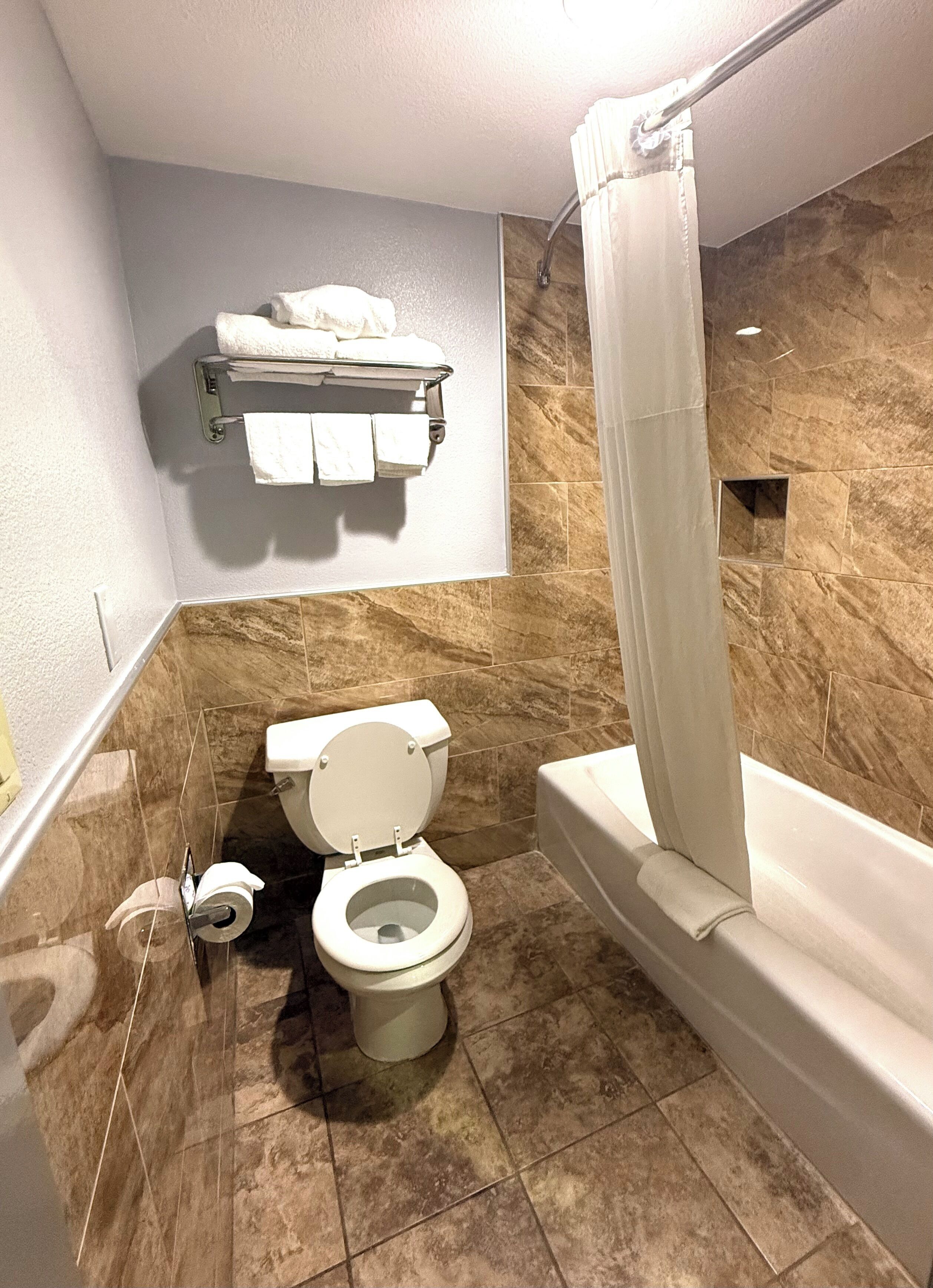 Une salle de bain comprenant des toilettes, une douche avec un rideau et un porte-serviettes avec des serviettes.