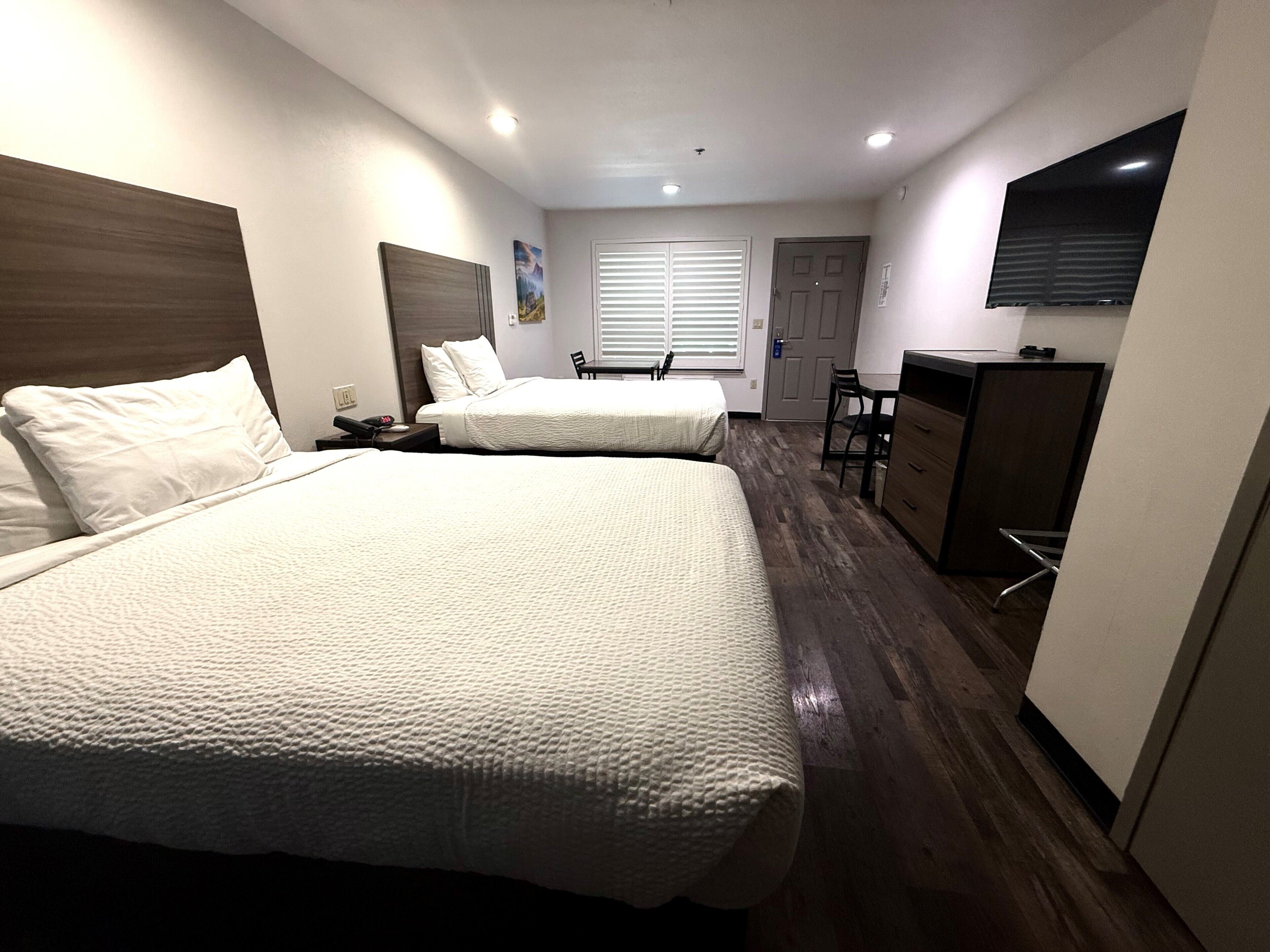 Une chambre d’hôtel avec deux lits, un bureau, une chaise, une télévision et une fenêtre avec des stores.