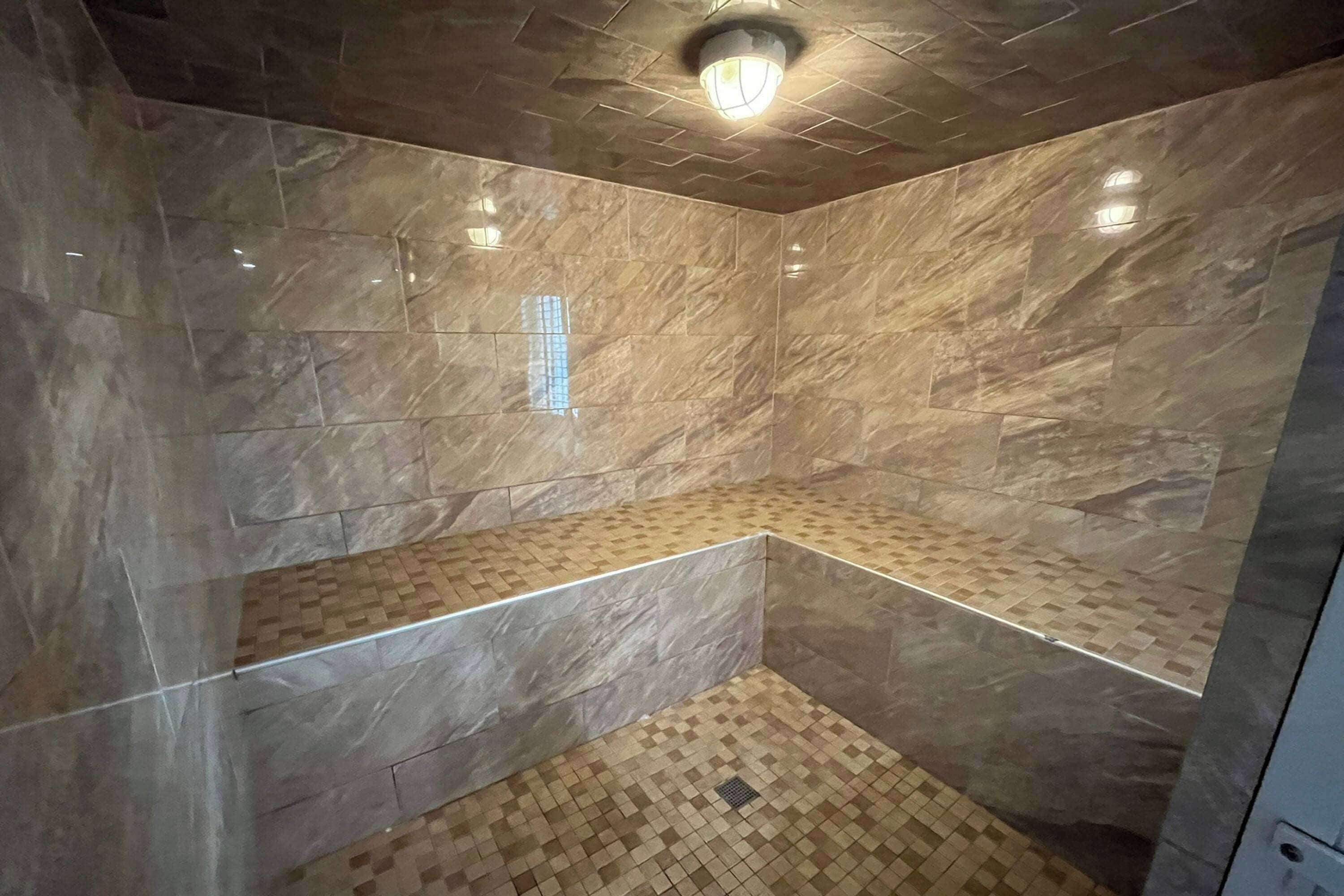 A corner shower with marble walls and a checkered floor.