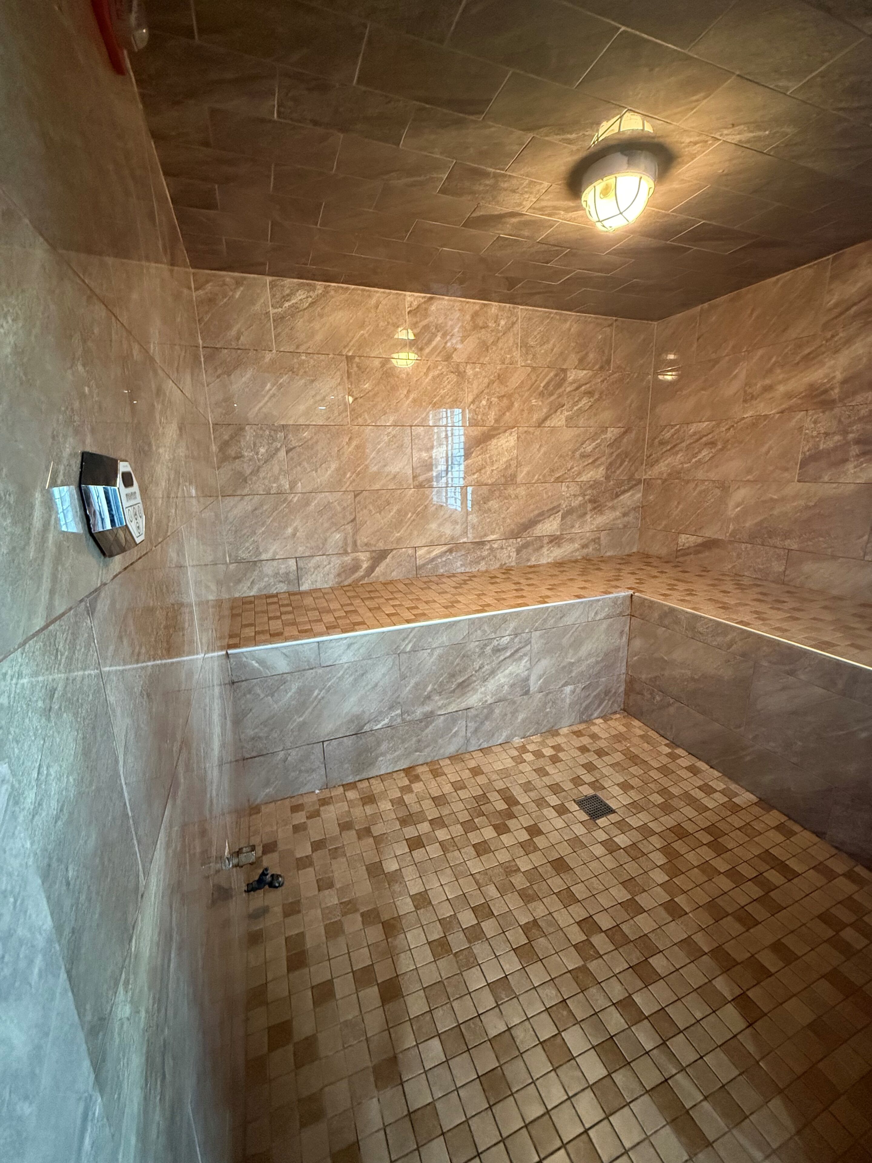 A bathroom with a tiled floor, a bench, and a wall-mounted light fixture.