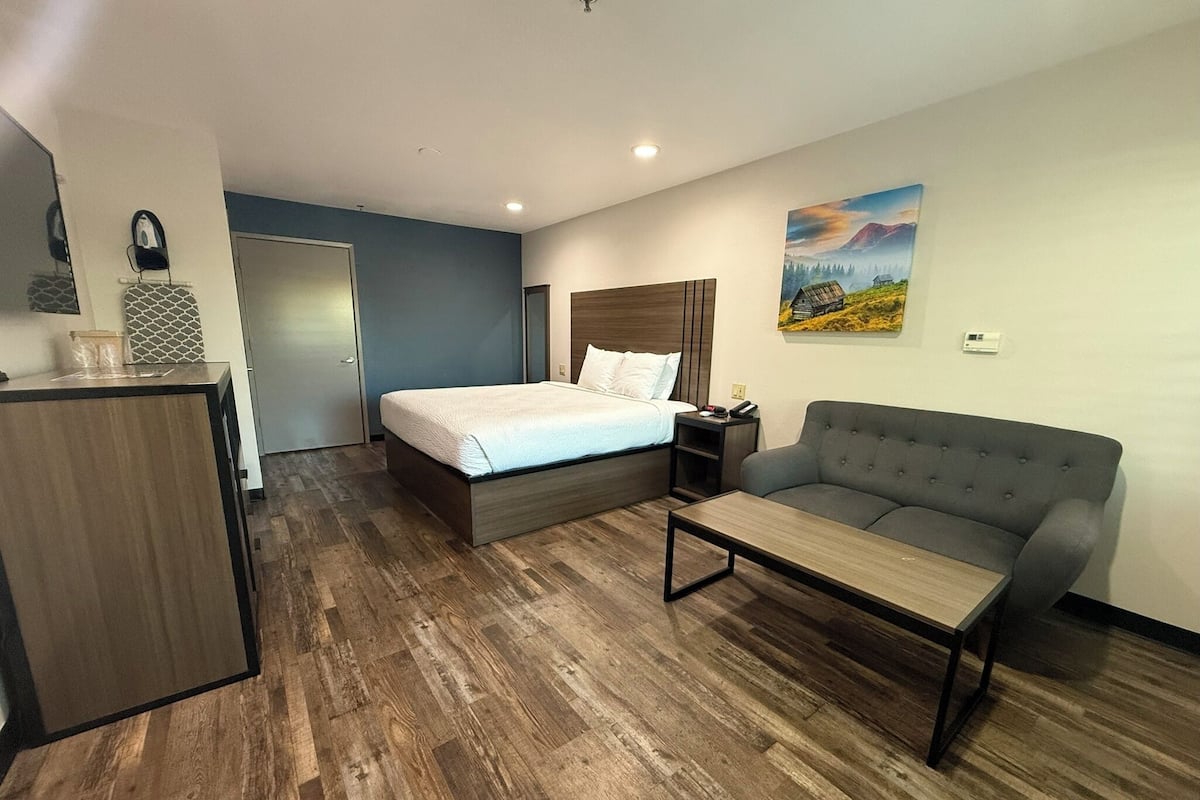 A hotel room with a bed, a sofa, a desk, and a painting on the wall.