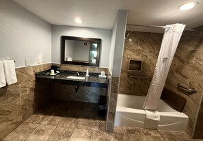 Une salle de bain avec un lavabo en marbre, un grand miroir, une douche avec un rideau et une baignoire.