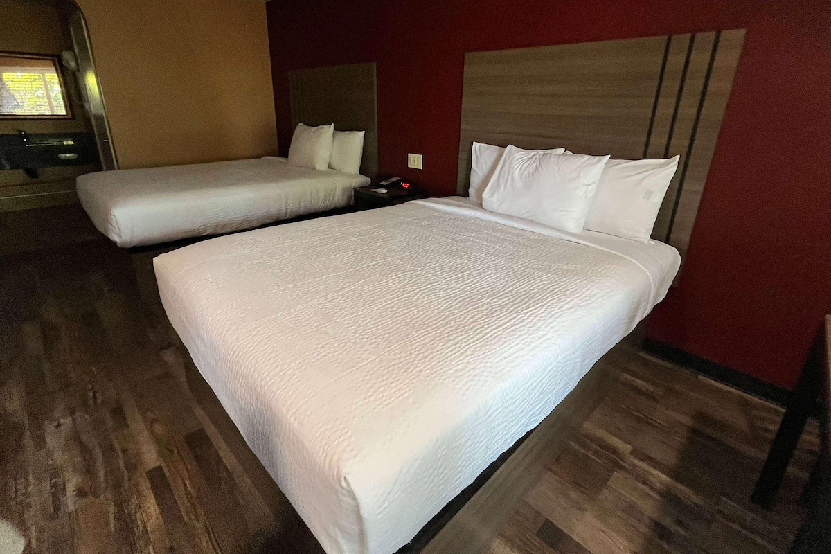 Quarto de hotel com duas camas, piso de madeira e parede vermelha.