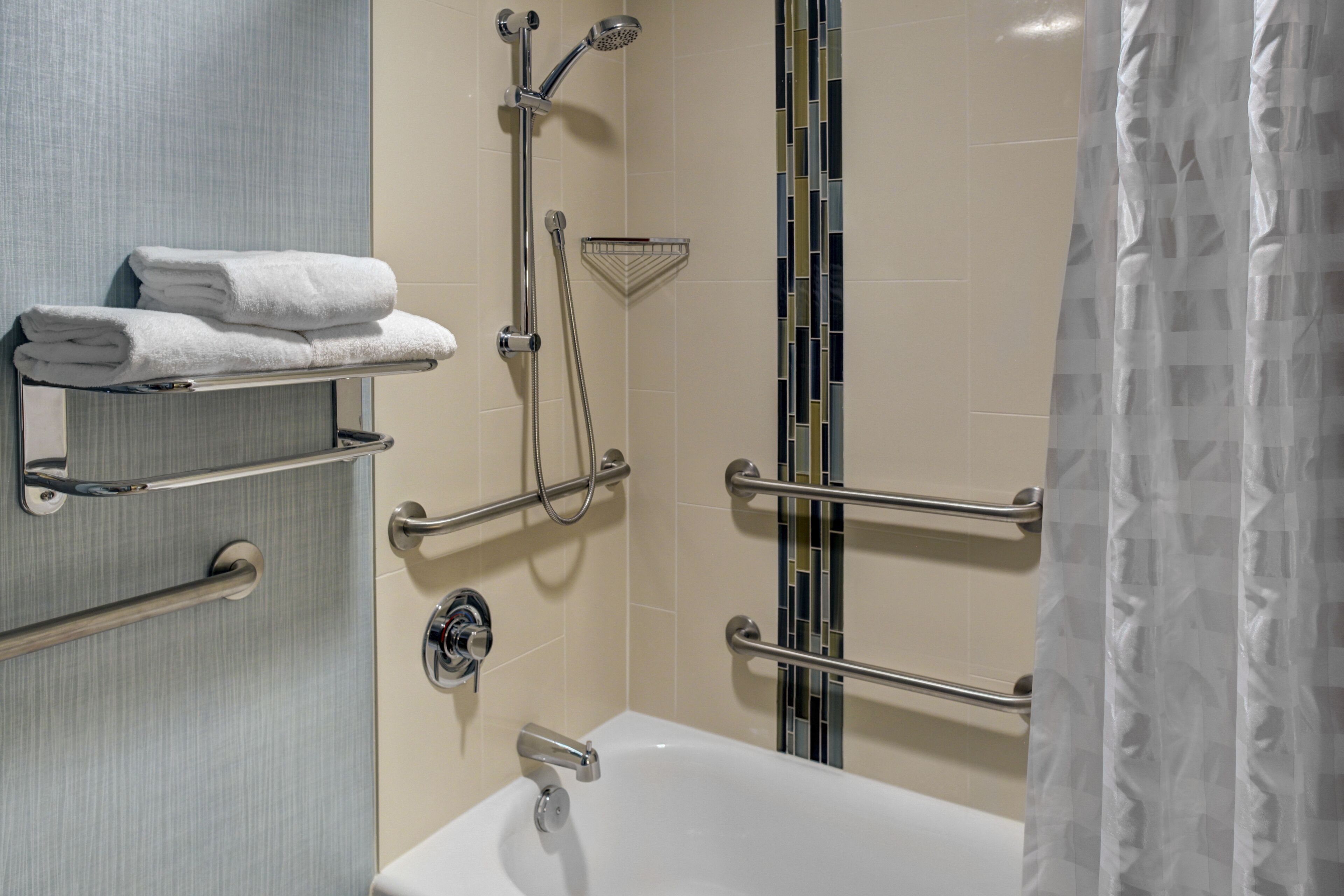 A bathroom with a bathtub, a shower with a handheld showerhead, and a towel rack with folded towels.