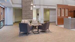 A modern hotel lobby with a reception desk, seating area with a table and chairs, and a large wooden accent wall. - Candlewood Suites Birmingham - Inverness by IHG (Birmingham)