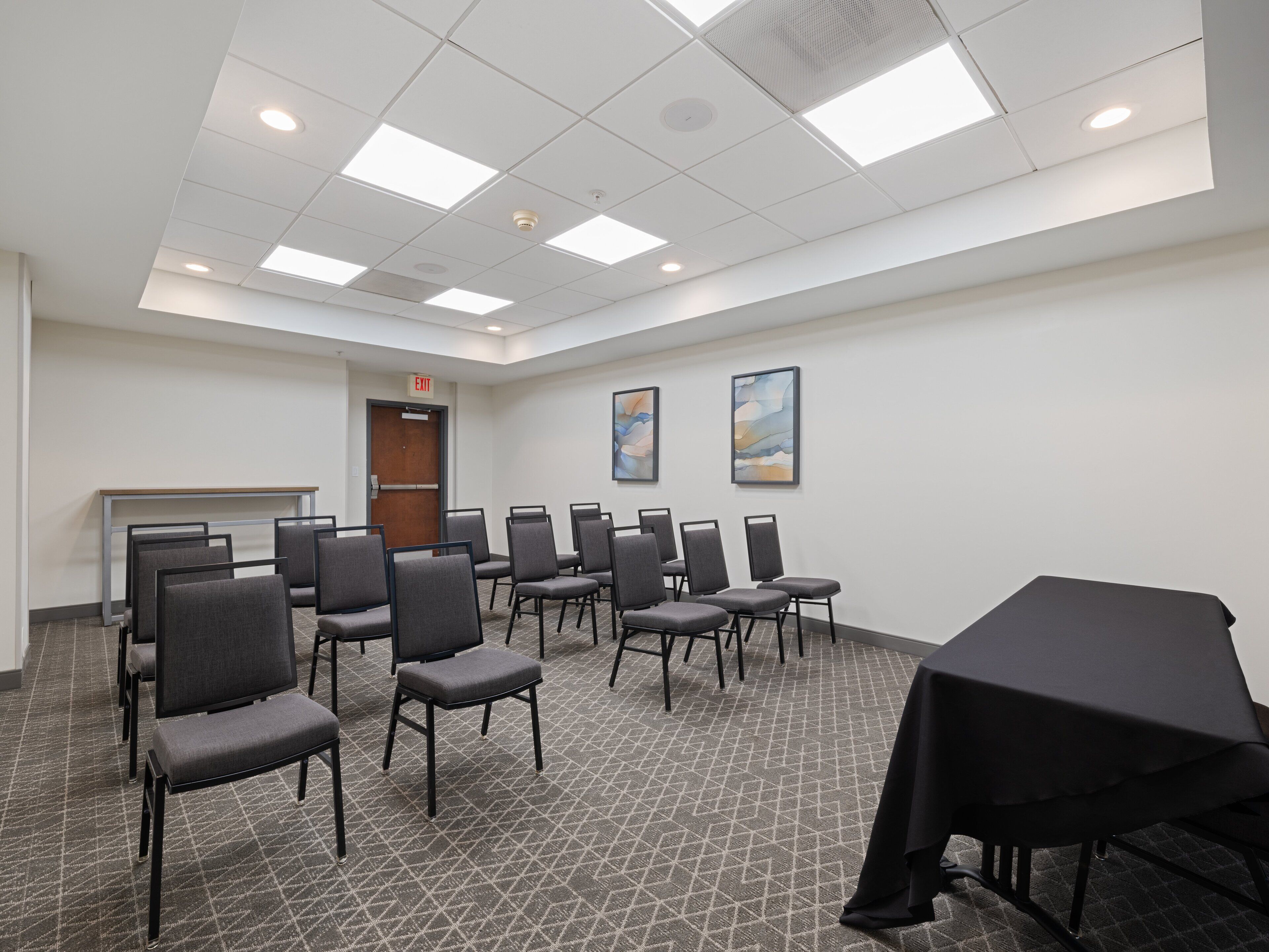 A conference room with a long table, several chairs, a carpeted floor, and a door marked "EXIT".