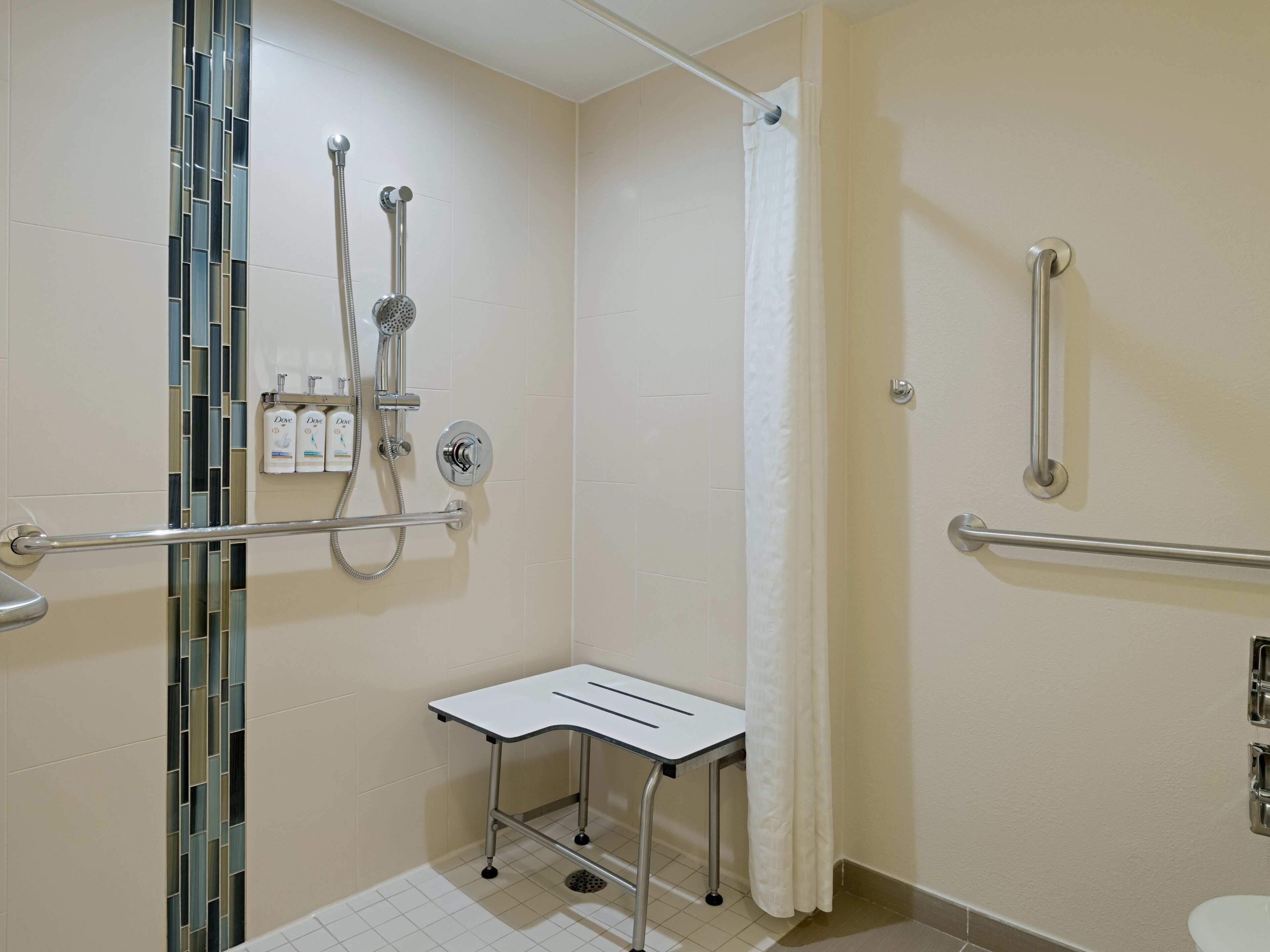 A bathroom with a shower, grab bars, a white sink, and a tiled floor.