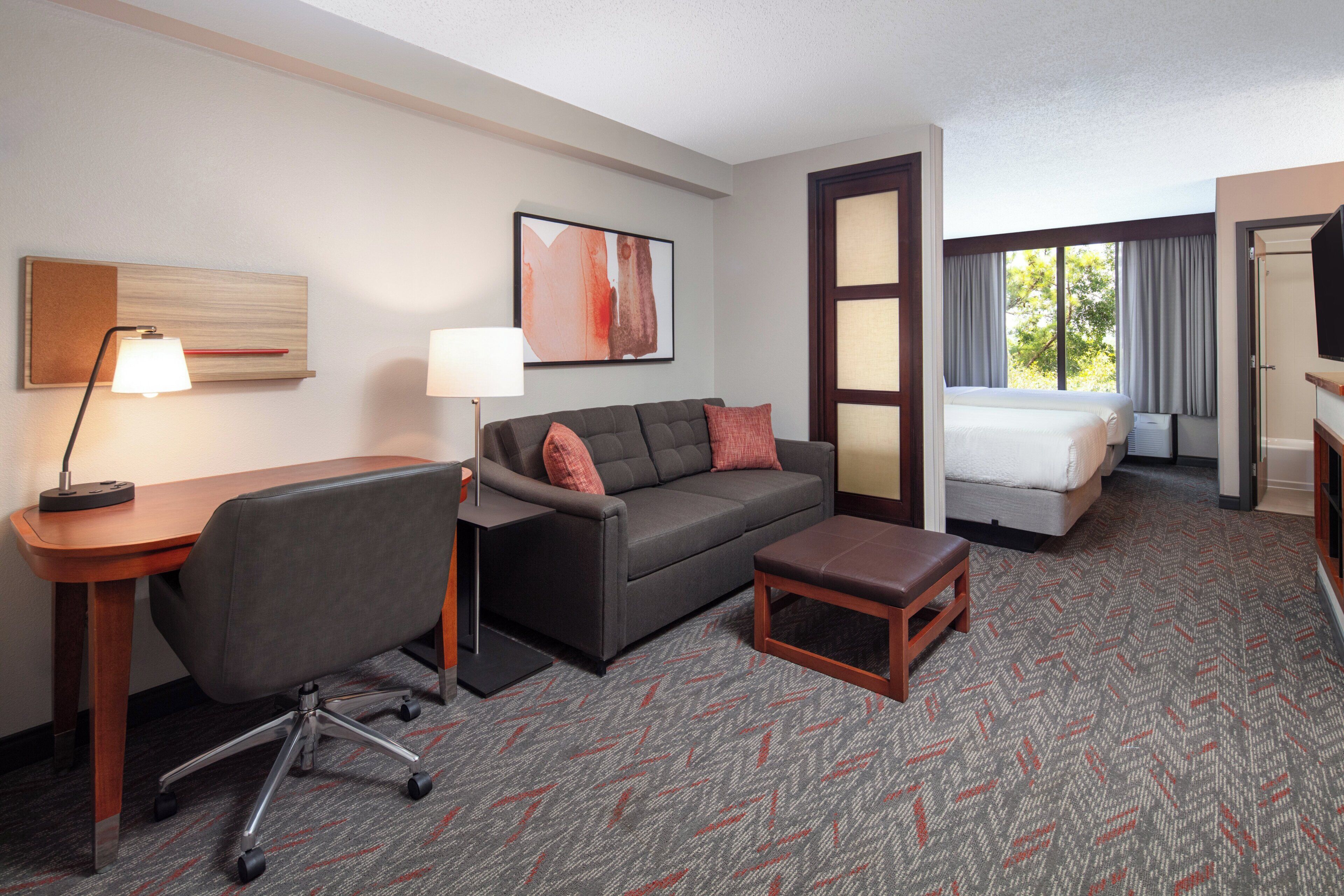 A hotel room with a desk, office chair, sofa, and a bed.