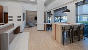 A modern hotel lobby with a reception desk, seating area, and a large dining space with a view. - Candlewood Suites Birmingham - Inverness by IHG (Birmingham)