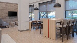 A modern interior with a dining area, large windows, and a flat-screen TV mounted on a wooden wall. - Candlewood Suites Birmingham - Inverness by IHG (Birmingham)