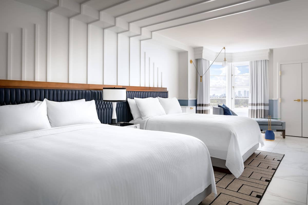 A hotel room with two beds, a modern design, a city view, and a large window.
