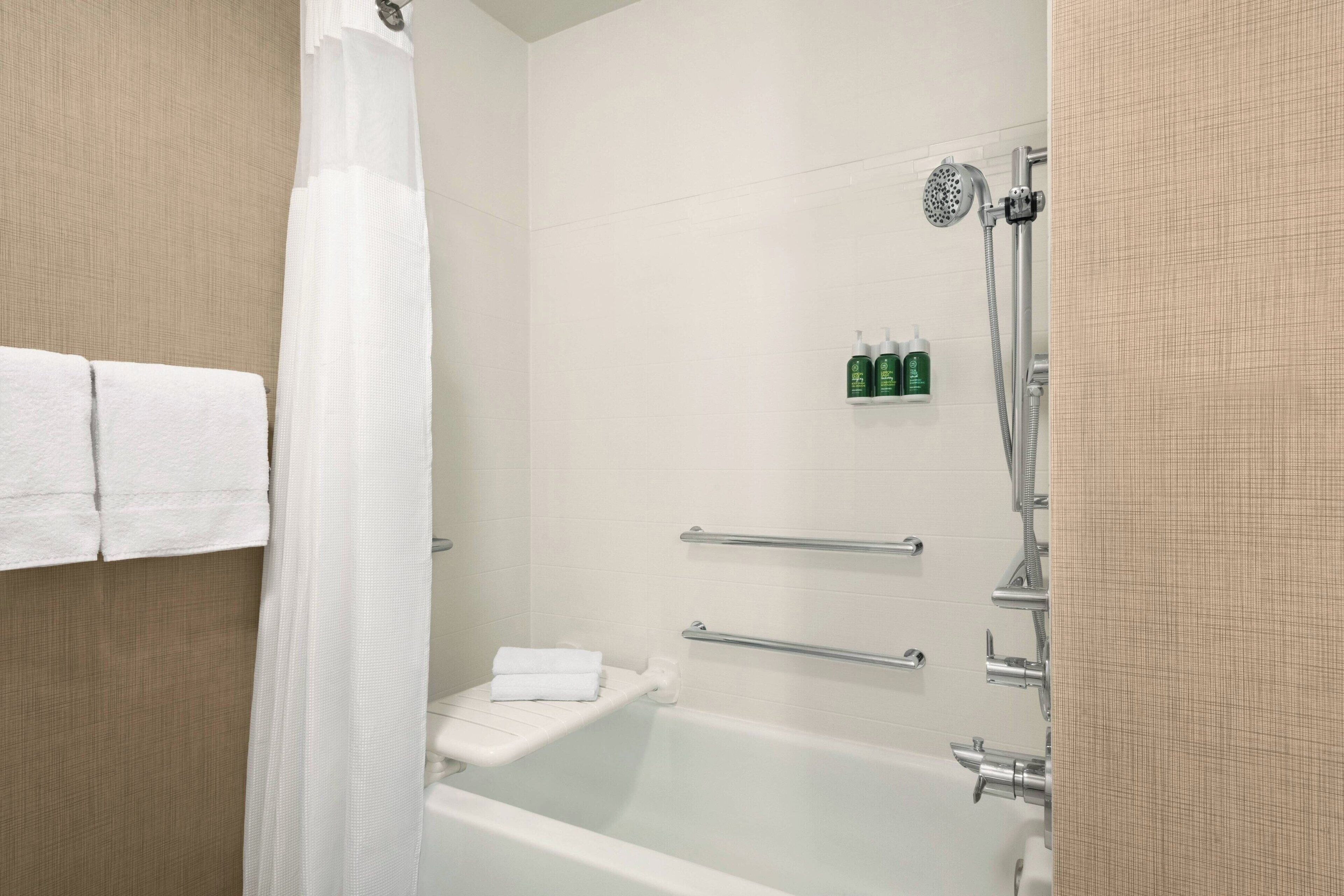 A modern bathroom with a bathtub, a shower, and a toilet. There are two towel racks and a shelf with toiletries.