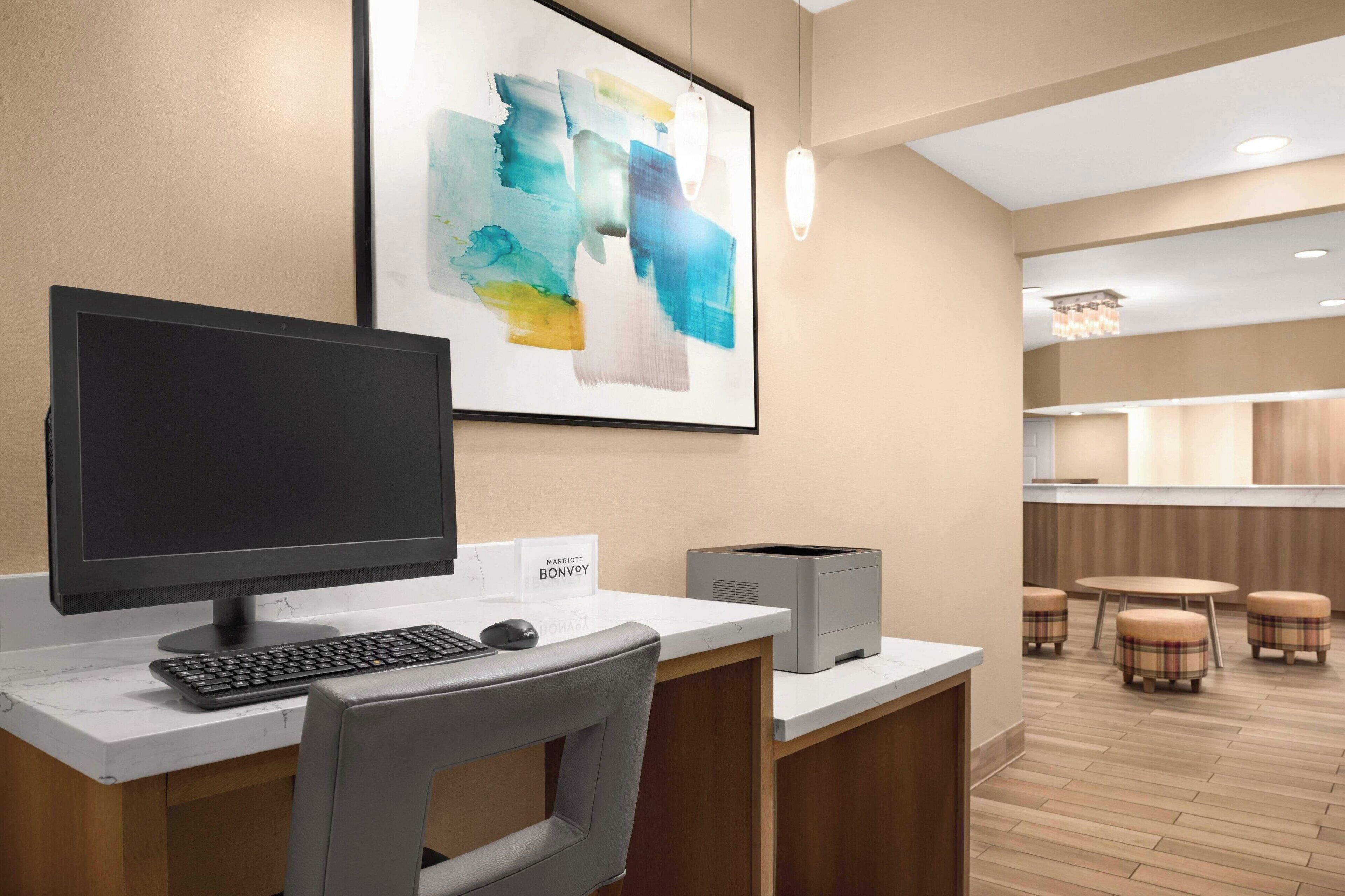 Un mostrador de recepción de hotel con una computadora, una impresora y un cuadro abstracto enmarcado en la pared.
