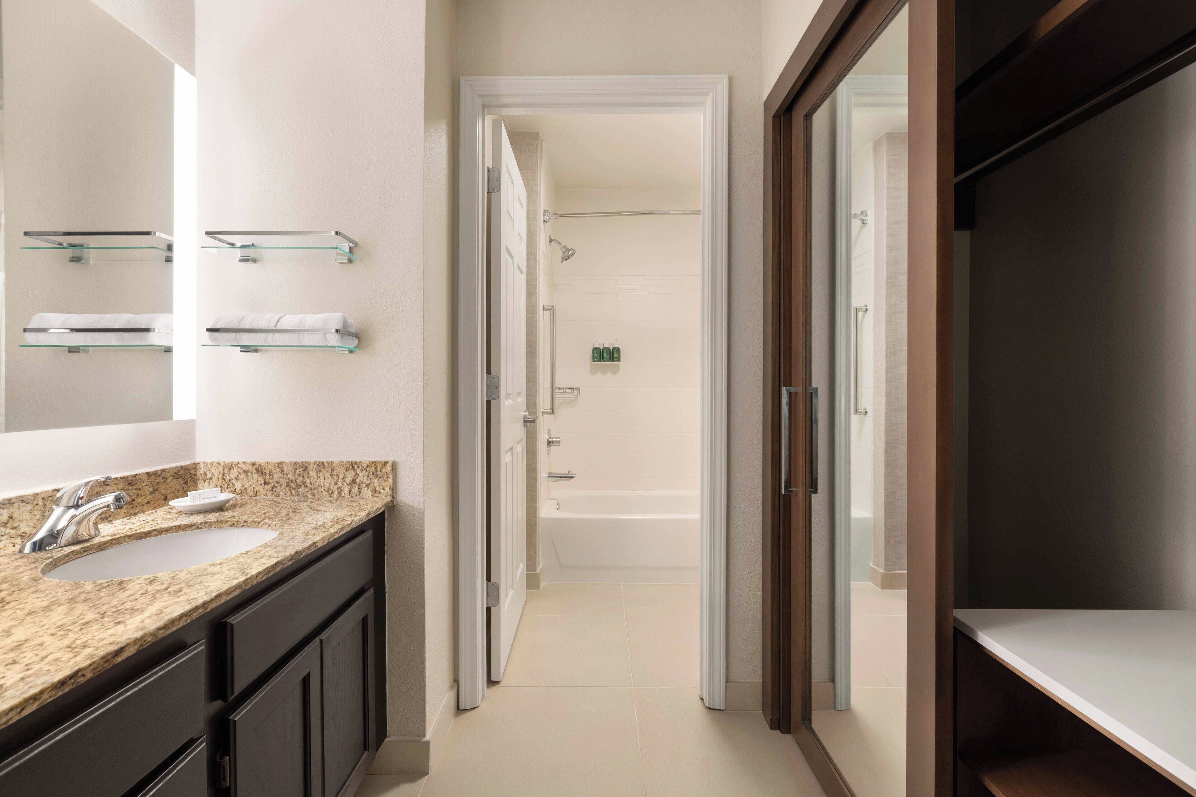 A modern bathroom with a granite countertop sink, a large mirror, and a walk-in shower.